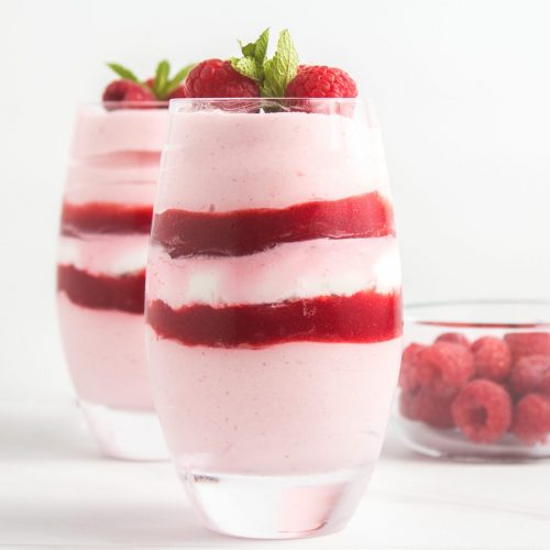 Two pink raspberry mousse cups in large curved glass tumblers.